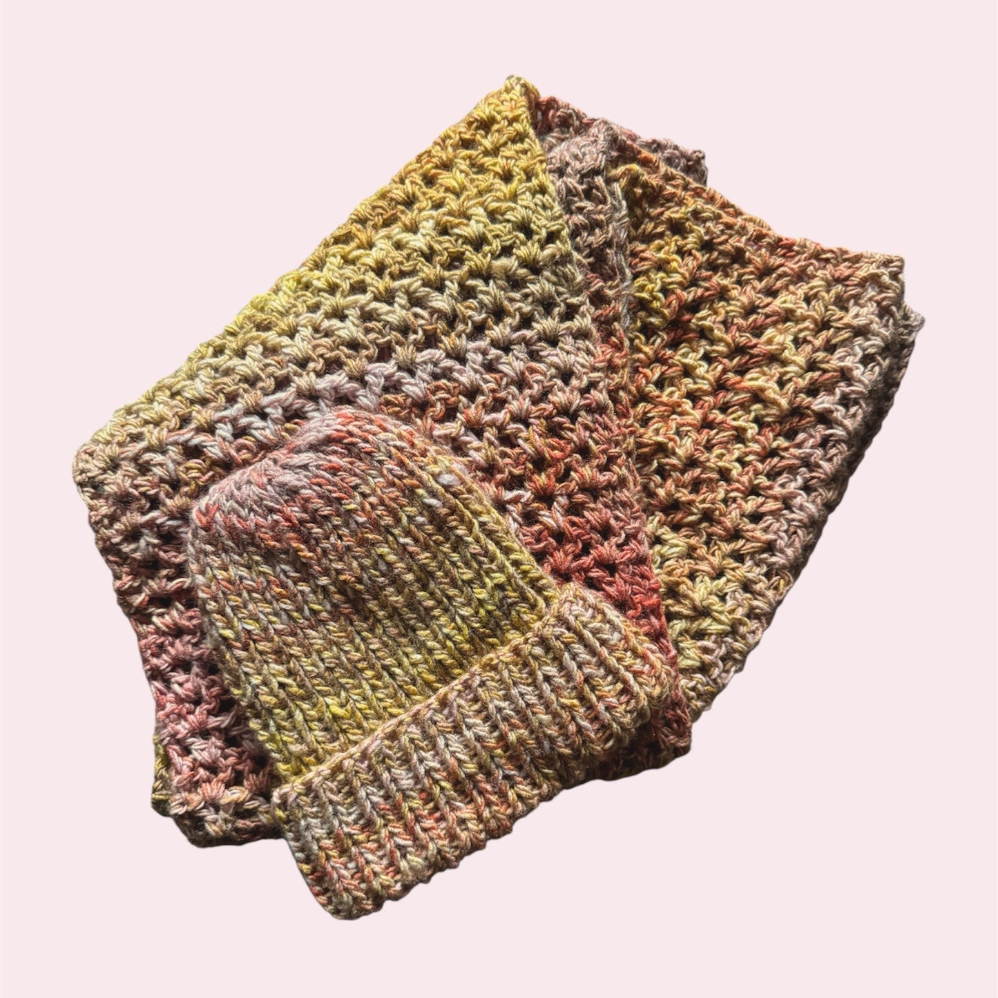 Crochet scarf and knitted beanie in a gradient of pink, yellow and orange, flatlay on a pink background