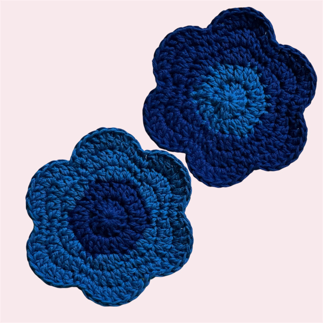 Blue flower-shaped crochet coasters on a pink background