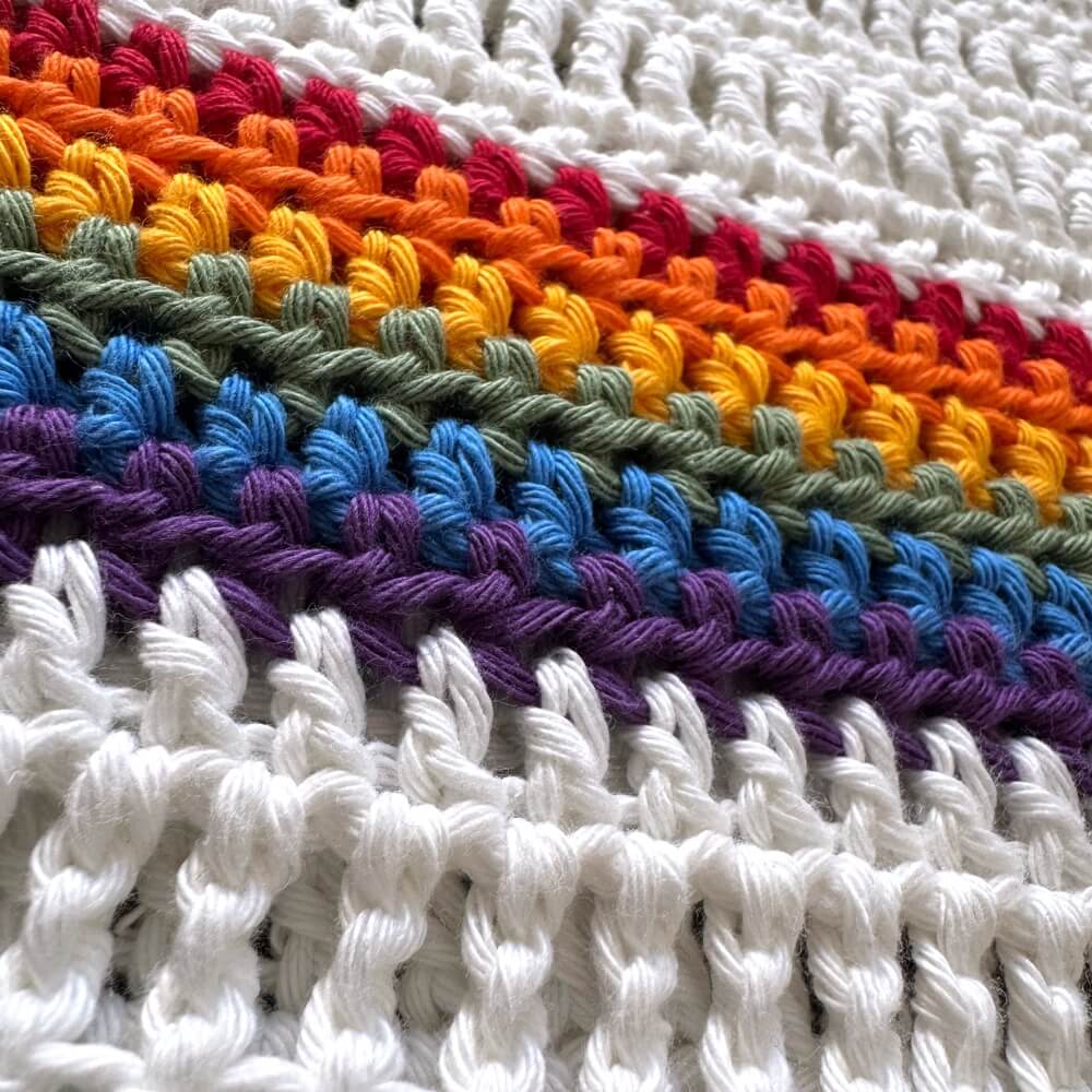 Close-up of white crochet pride tee with a rainbow pattern