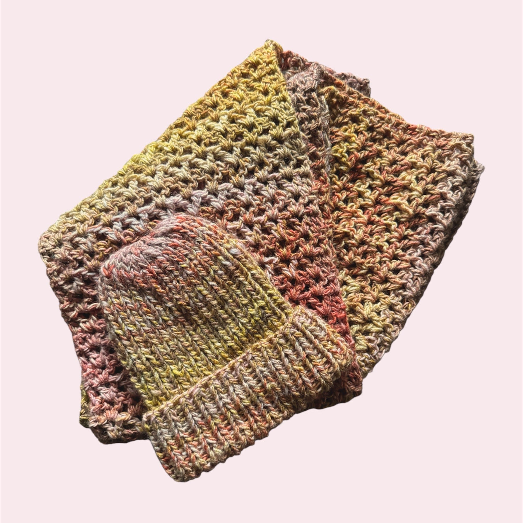 Crochet scarf and knitted beanie in a gradient of pink, yellow and orange, flatlay on a pink background