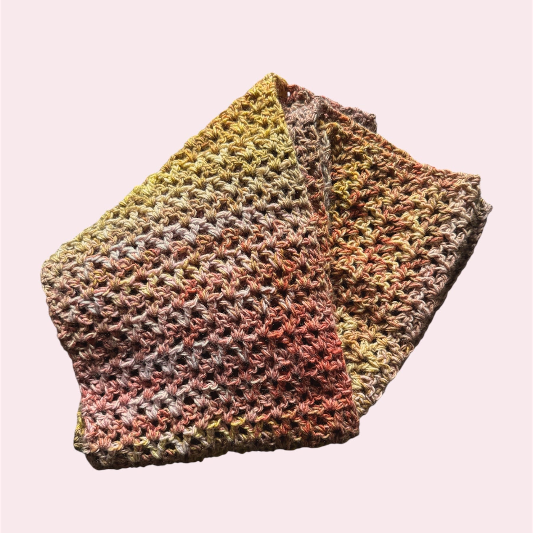 Crochet scarf in a gradient of yellow, pink and orange, flatlay on a pink background