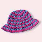 Crocheted bi pride bucket hat with pink, blue and purple colors on a light pink background.