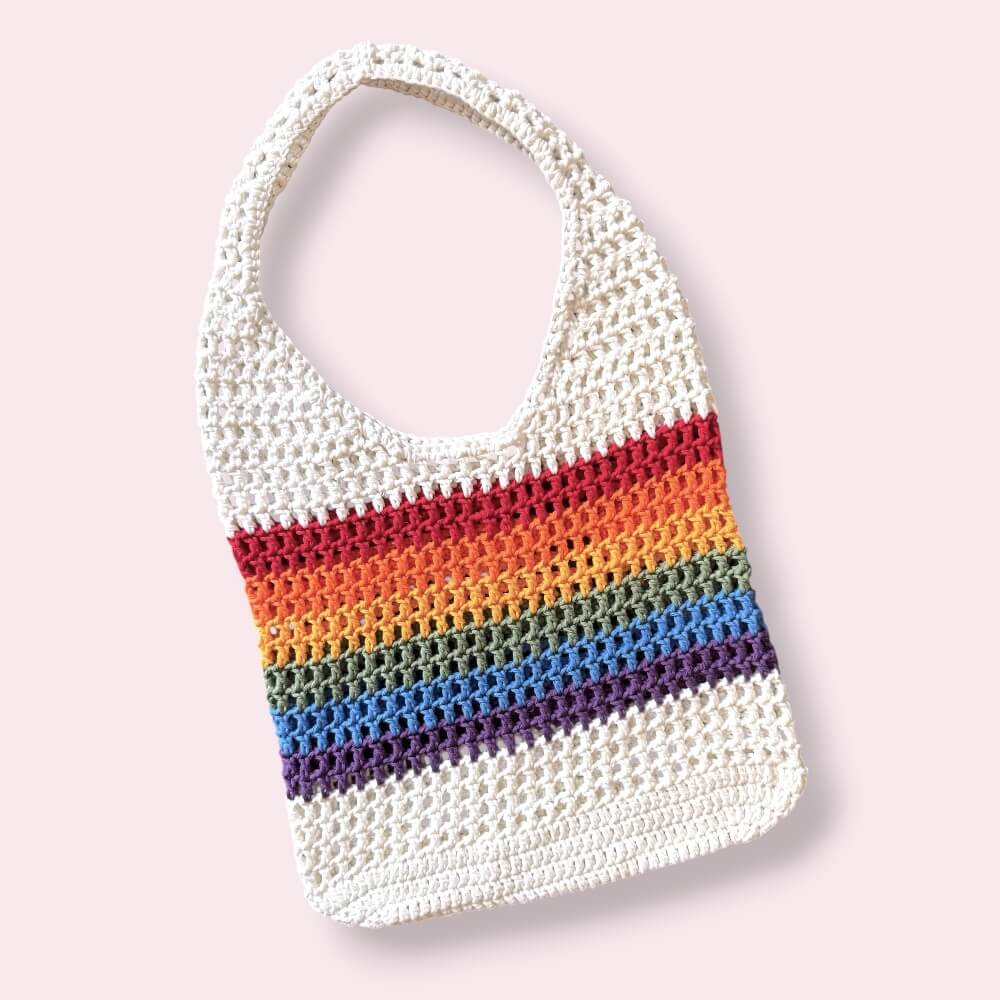 Crocheted mesh tote bag with rainbow stripes on a light pink background