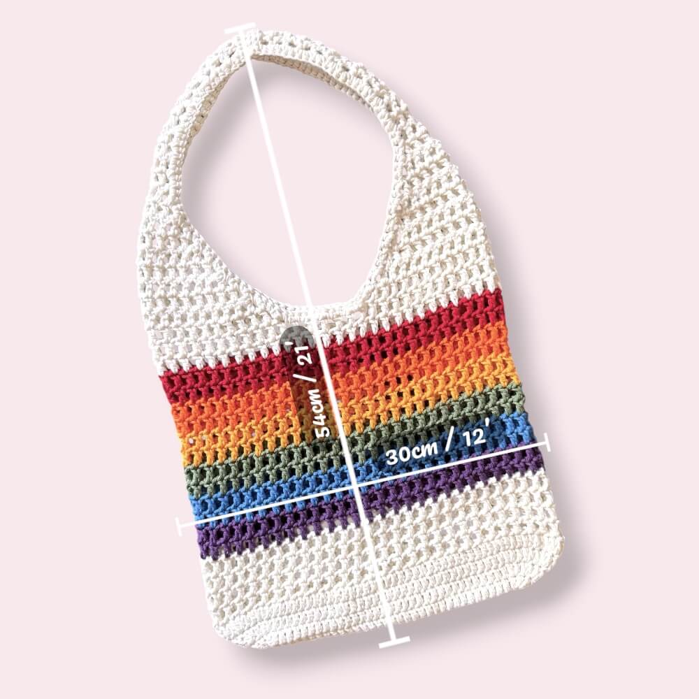 Crocheted mesh tote bag with rainbow stripes with measurements on a light pink background