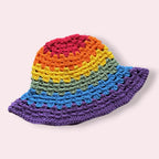 Crocheted rainbow bucket hat with red, orange, yellow, green, blue, and purple colors on a light pink background.
