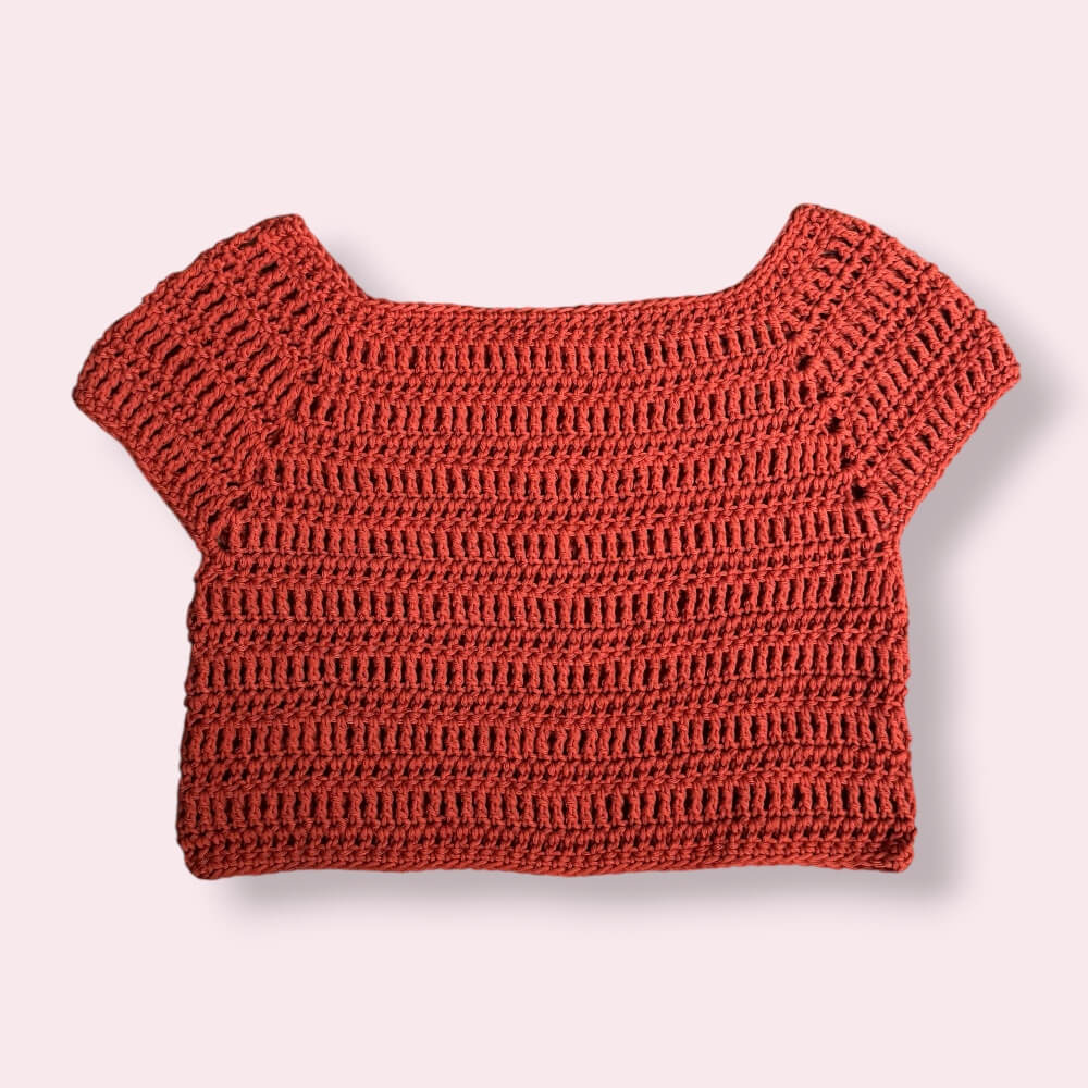 Flatlay of crochet orange tee on plain background