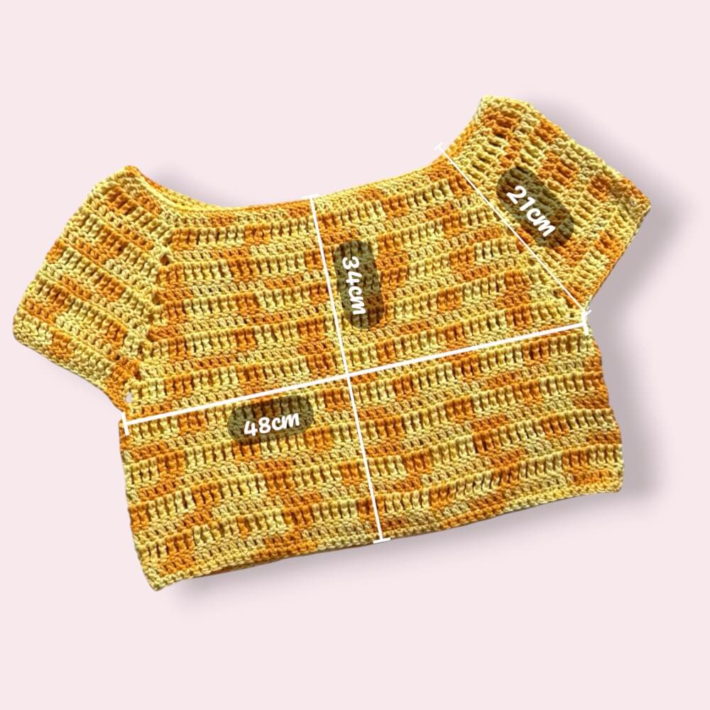 Flatlay of yellow crochet tee on plain background with measurements