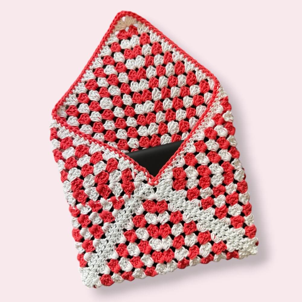 Open crocheted white and coral kindle sleeve on plain background