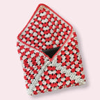 Open crocheted white and coral kindle sleeve on plain background