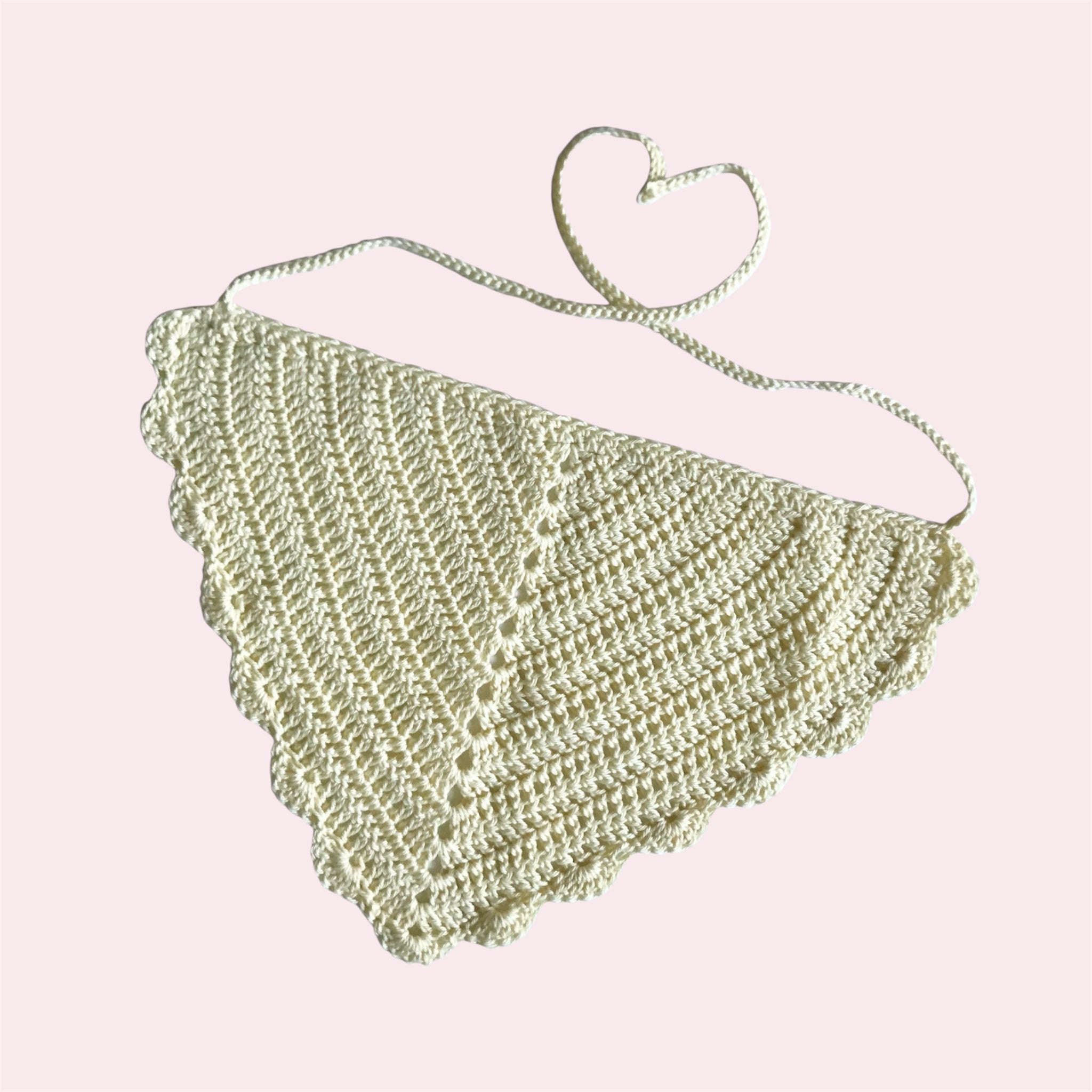 Pastel yellow crochet bandana with scalloped edges on a light pink background
