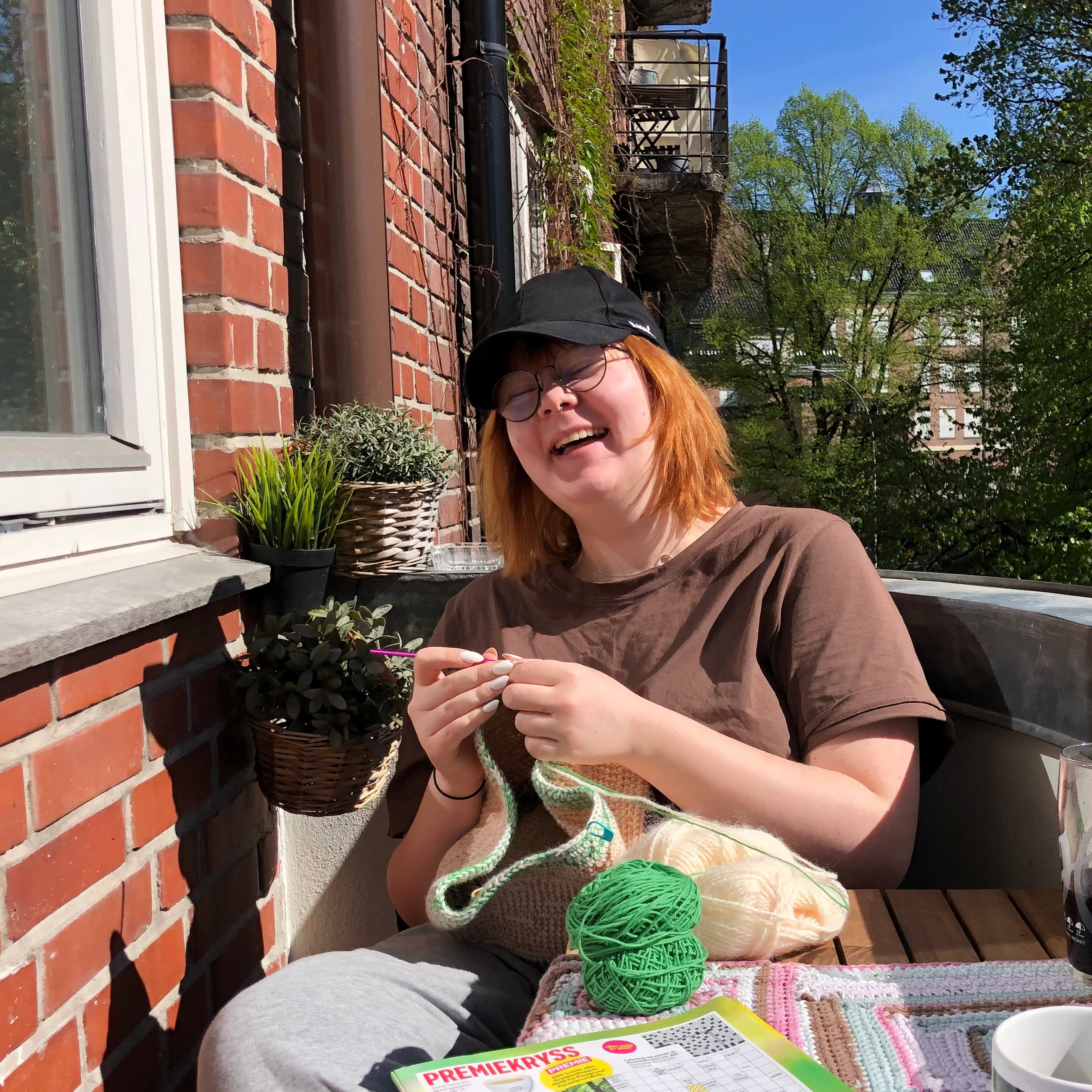 Person crocheting on a balcony in the sun laughing