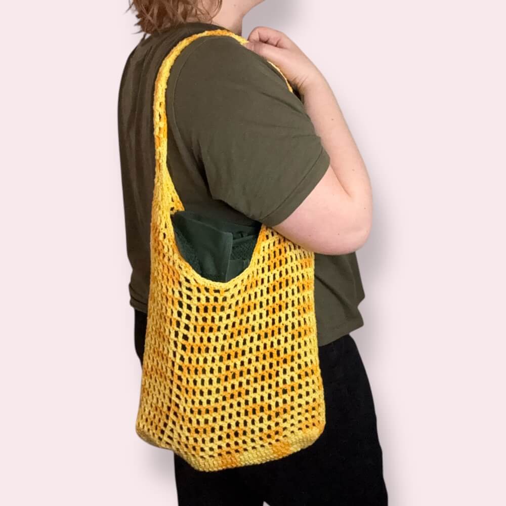 Person holding a yellow mesh bag over their shoulder on a plain background