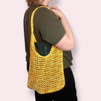 Person holding a yellow mesh bag over their shoulder on a plain background