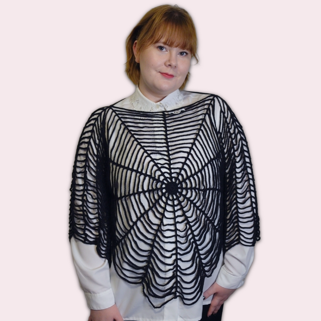 Person wearing a black spider web crochet shirt on a plain background