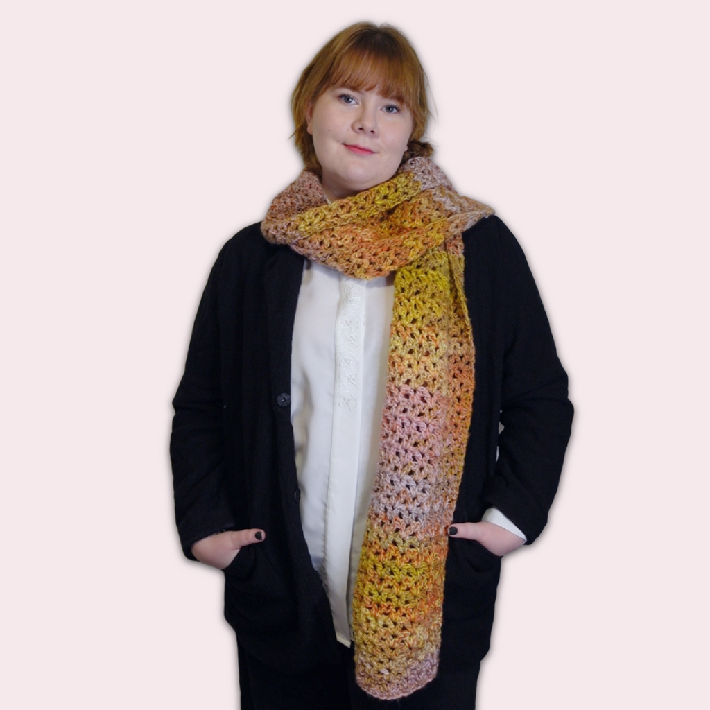 Person wearing a colorful crochet scarf on a pink background