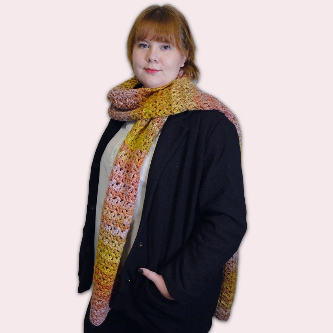 Person wearing a colorful crochet scarf on a plain background