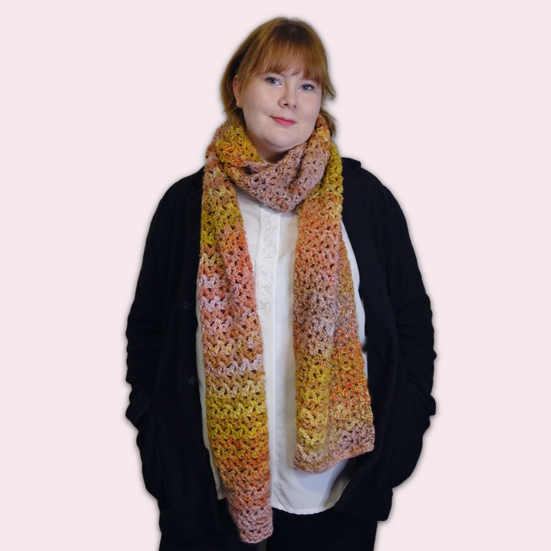 Person wearing a colorful crocheted scarf against a plain background