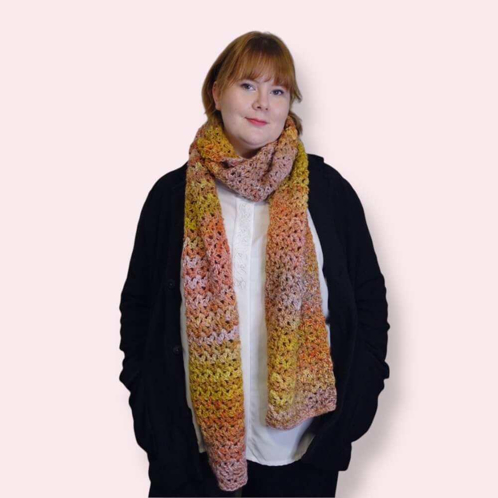 Person wearing a colorful crocheted scarf on a plain background