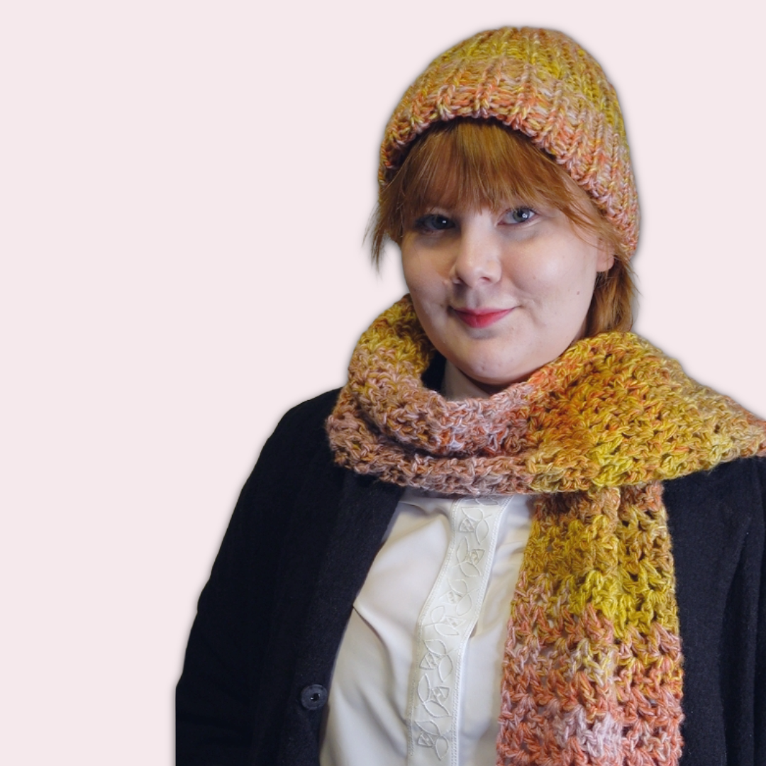 Person wearing a colorful knitted hat and crochet scarf on a plain background