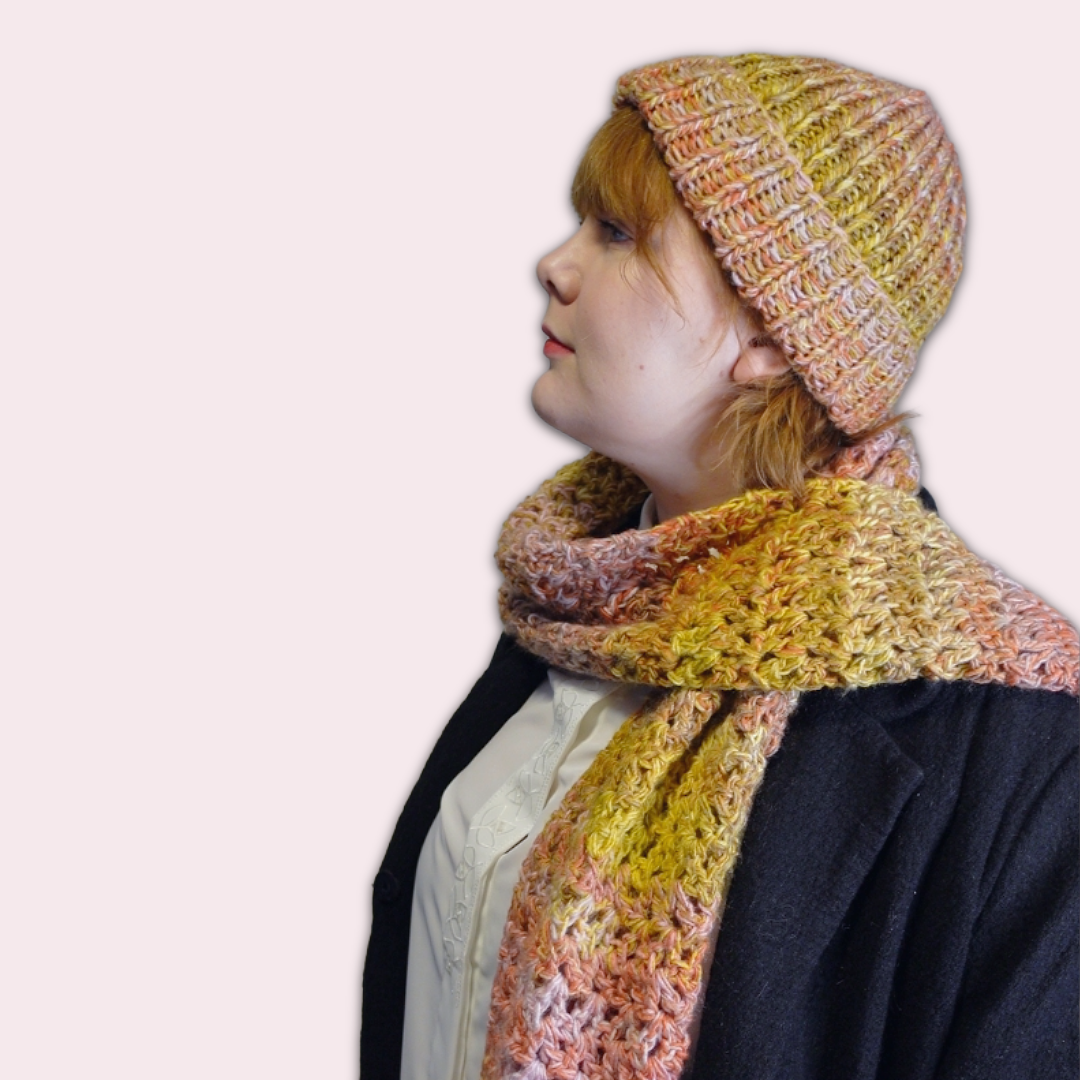 Person wearing a colorful knitted hat and crocheted scarf in side profile on a plain background