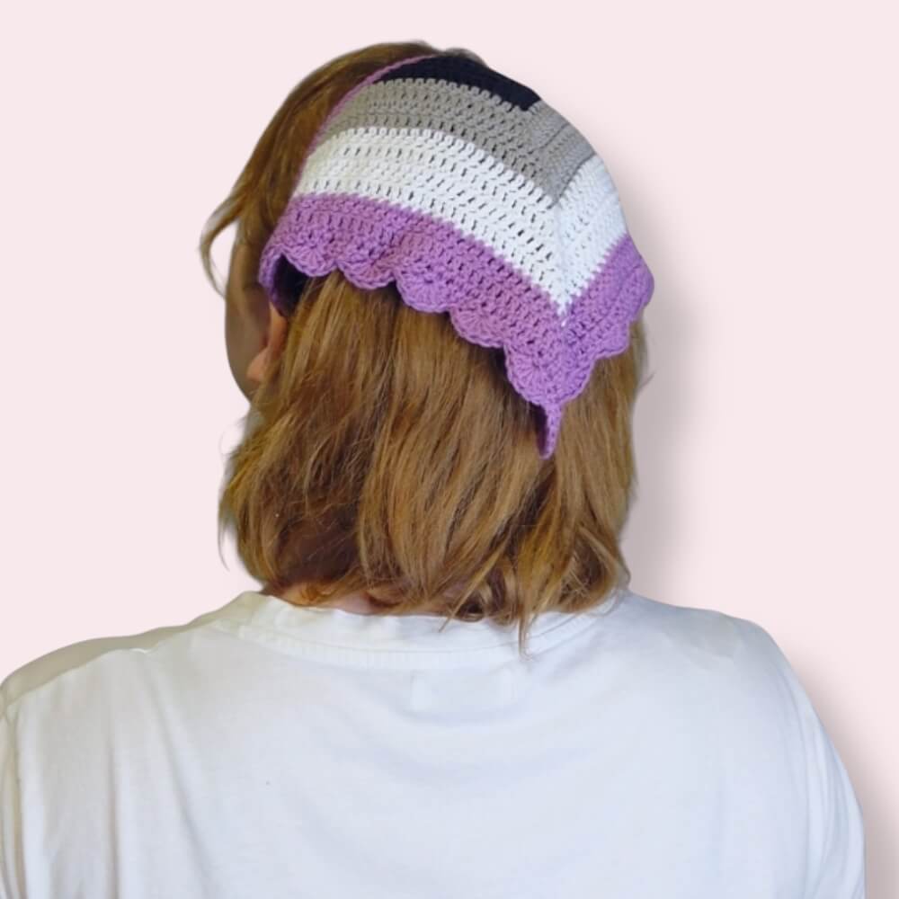 Person wearing a crochet bandana in ace pride colors on plain background 