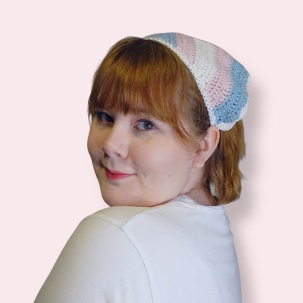 Person wearing a crochet bandana in trans pride colors on plain background
