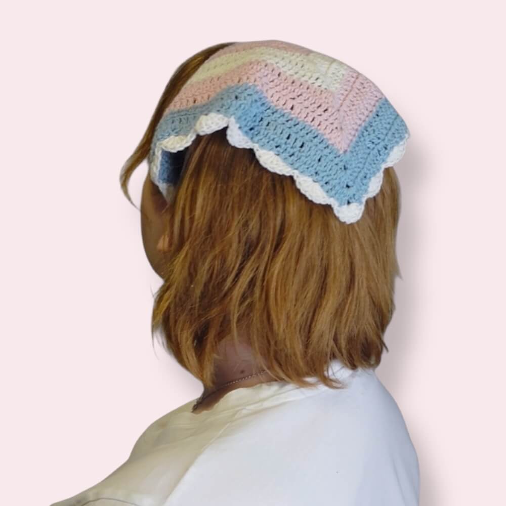 Person wearing a crochet bandana in trans pride colors on plain background back view