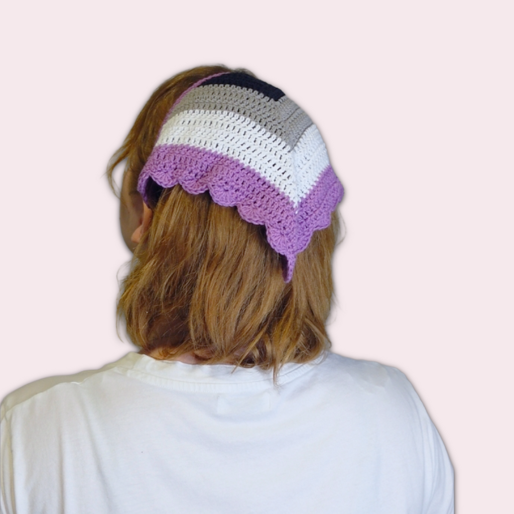 Person wearing a crochet bandana with ace pride colors on a light pink background.