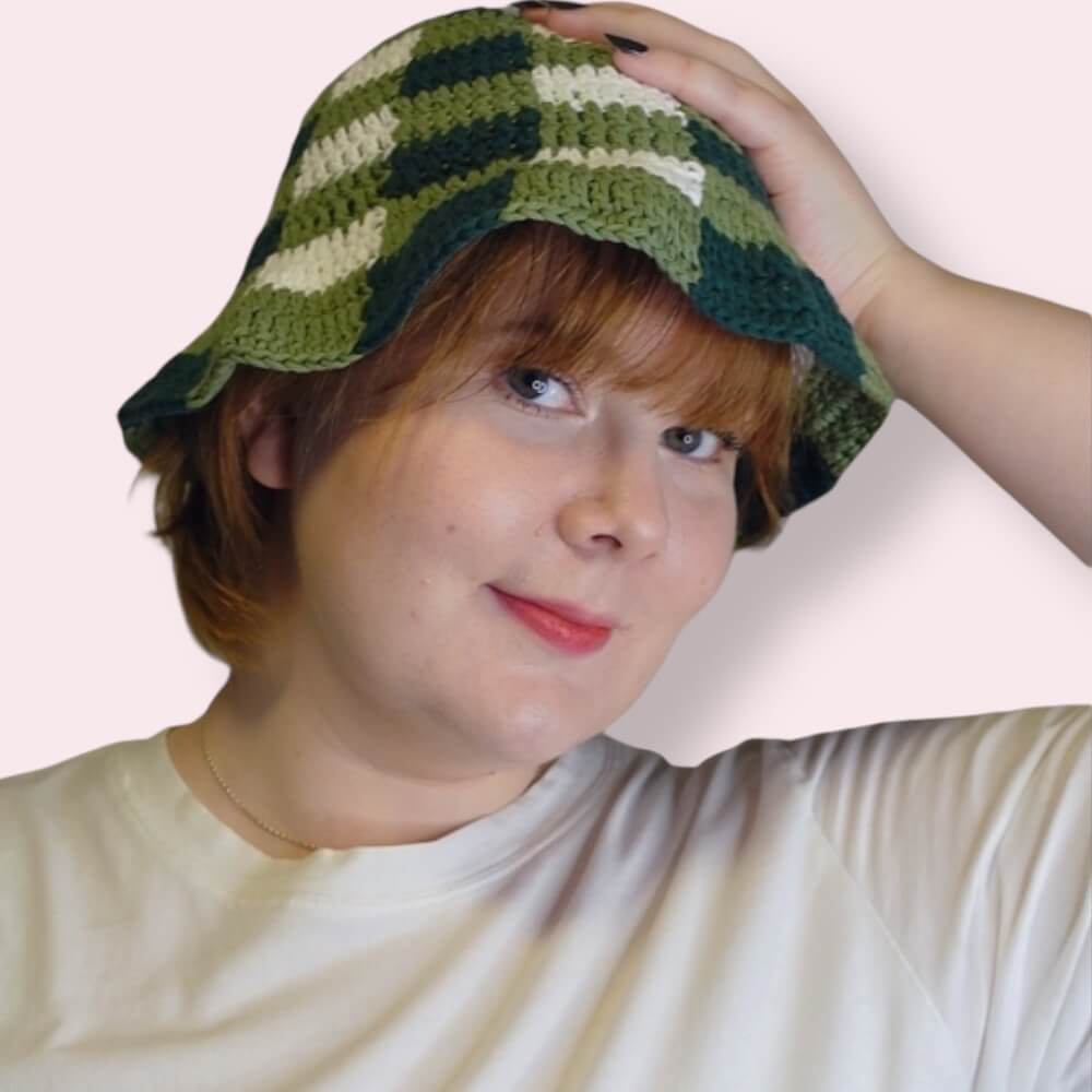 Person wearing a green and white checkered crochet bucket hat on a plain background