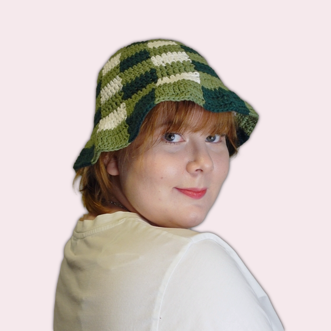 Person wearing a green and white checkered crochet bucket hat on a plain background