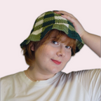 Person wearing a green and white checkered crochet bucket hat on a plain background