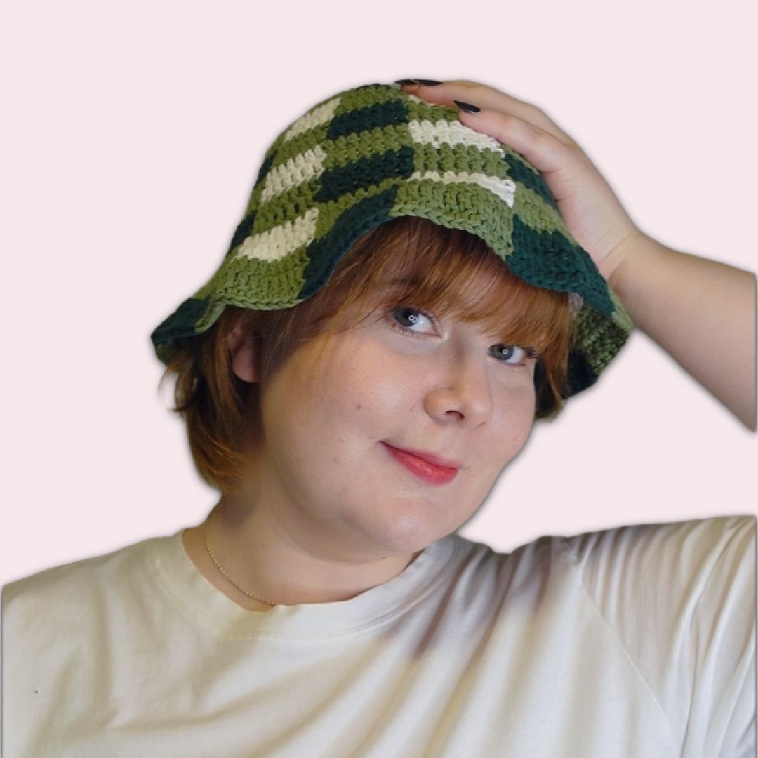 Person wearing a green and white checkered crochet bucket hat on a plain background