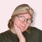 Person wearing a neutral multicolor crochet twisted earwarmer headband on a plain background