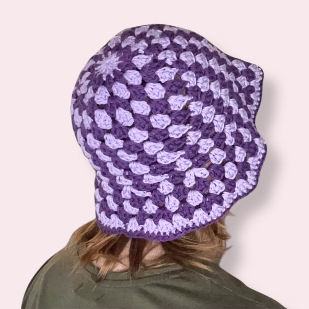 Person wearing a purple striped crochet bucket hat back view on a plain background