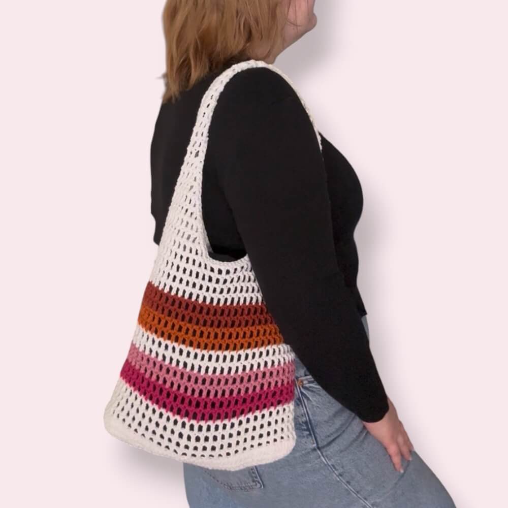 Person wearing a white and lesbian pride striped crochet bag on a plain background