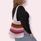 Person wearing a white and lesbian pride striped crochet bag on a plain background