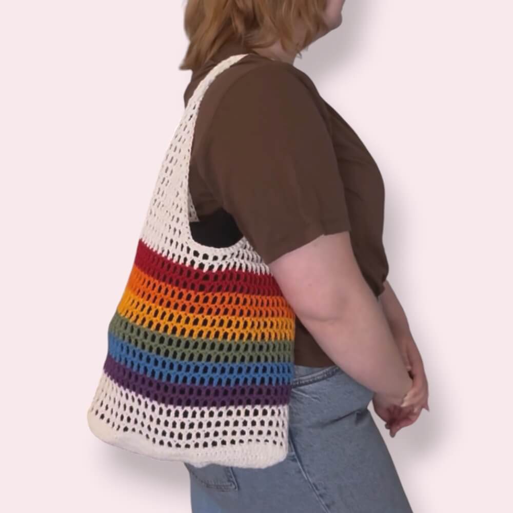 Person wearing a white and pride striped bag on a plain background