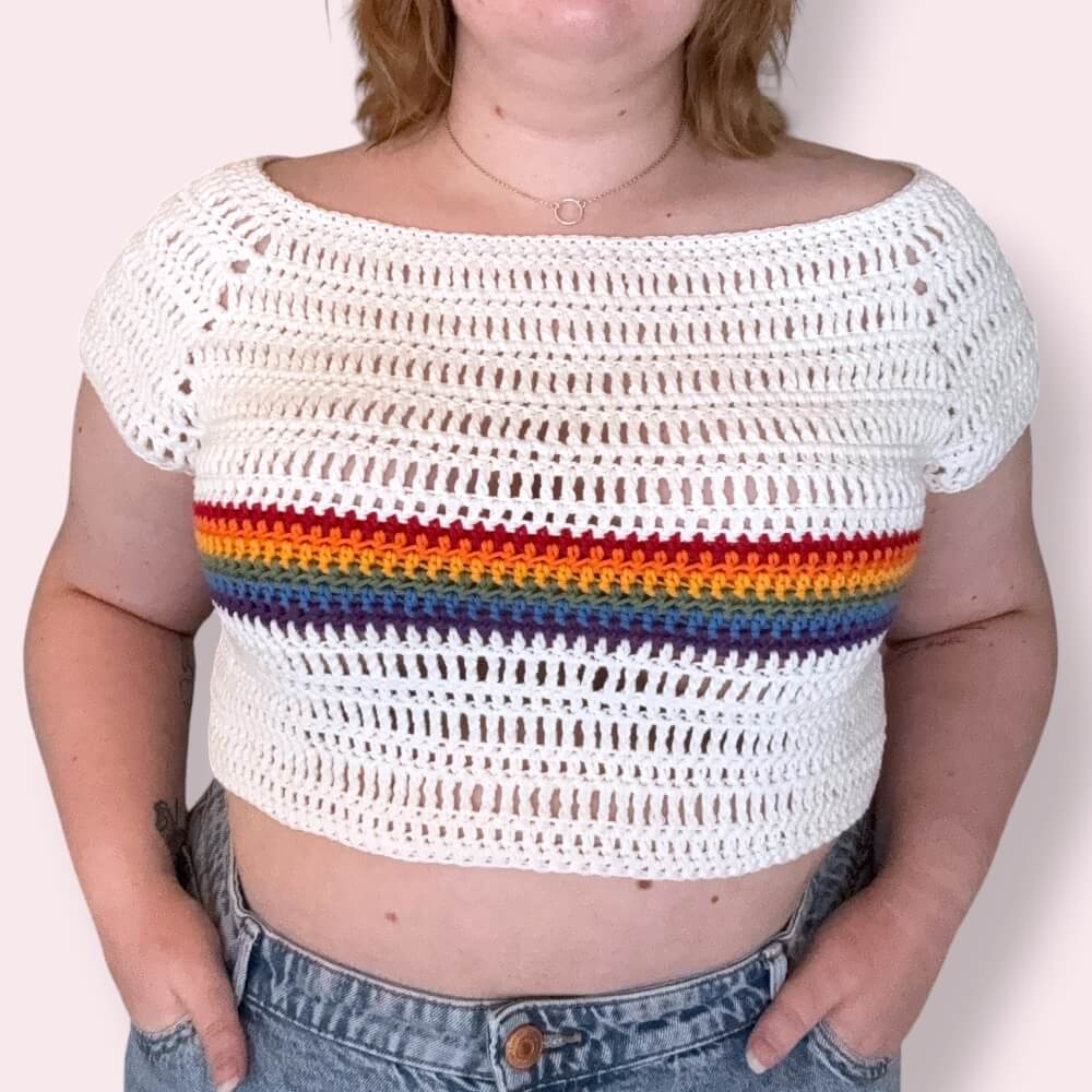 Person wearing a white crochet crop top with rainbow stripes on a plain background
