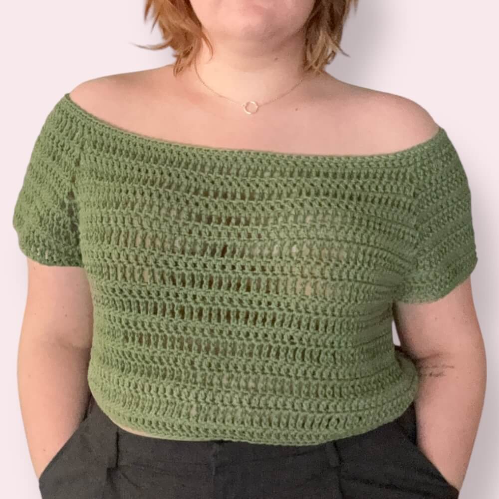 Person wearing an off-shoulder green crochet top against a plain background