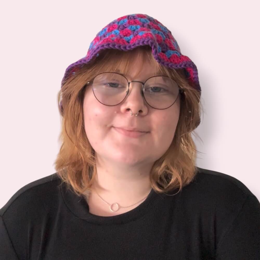 Person wearing bi pride crochet bucket hat in blue, pink and purple colors on plain background