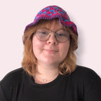 Person wearing bi pride crochet bucket hat in blue, pink and purple colors on plain background