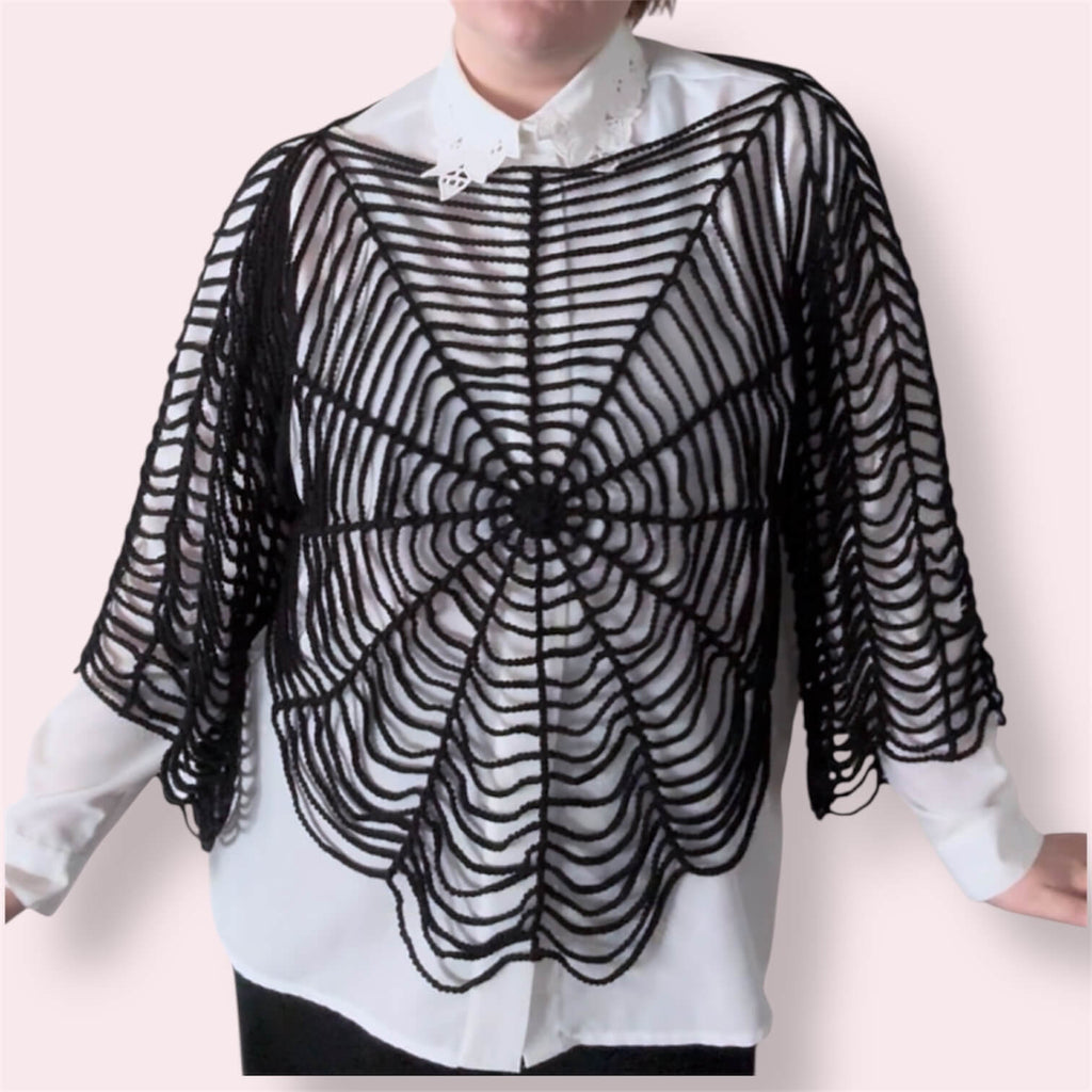 Person wearing black spiderweb top over white undershirt