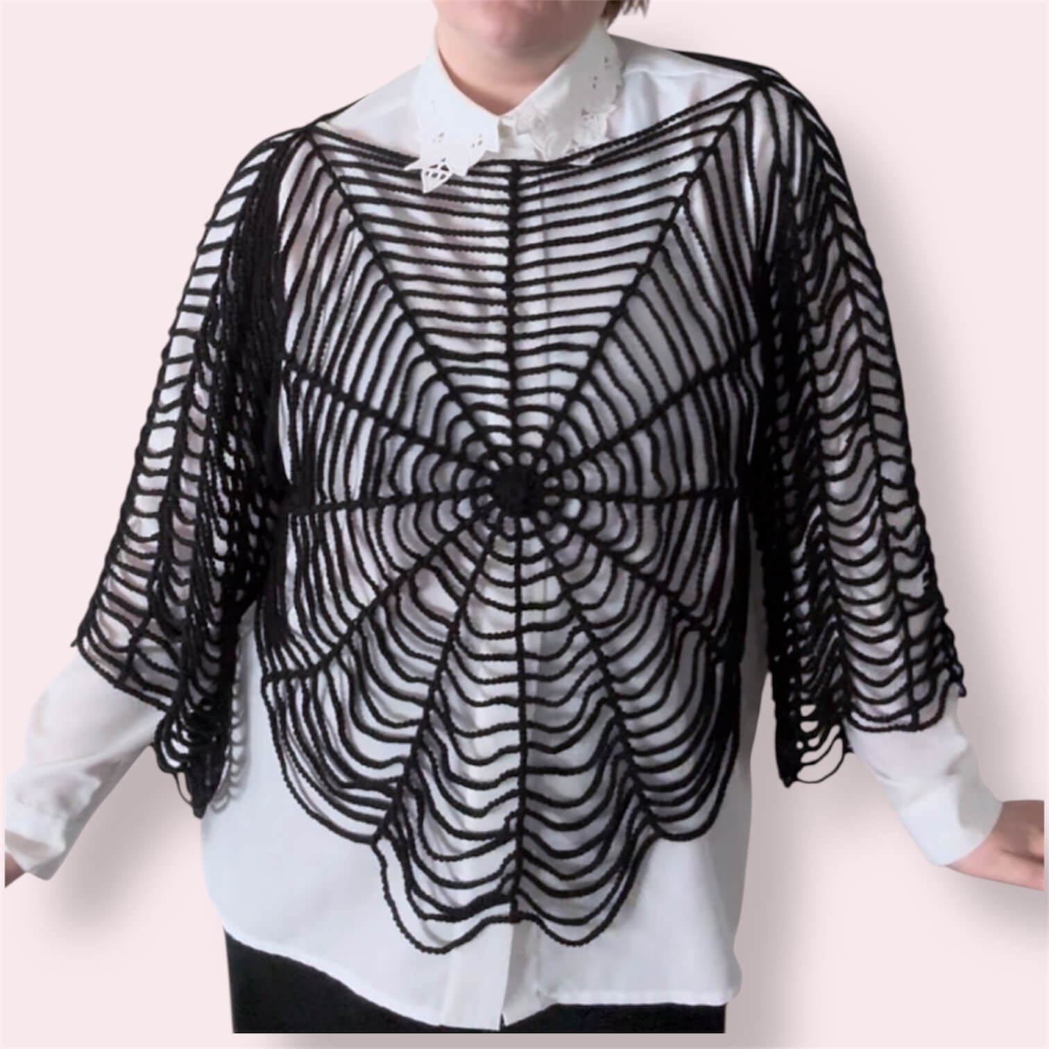 Person wearing black spiderweb top over white undershirt