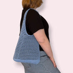 Person wearing blue crochet mesh tote bag on plain background
