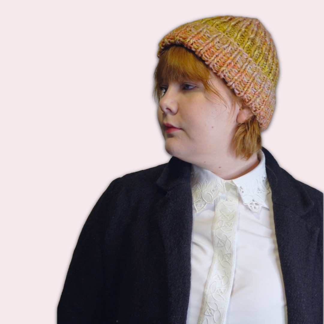 Person wearing colorful knit beanie in side profile on a plain background