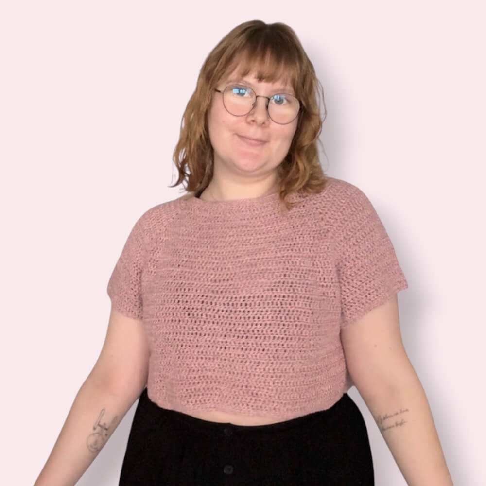 Person wearing pink crochet tshirt on plain background