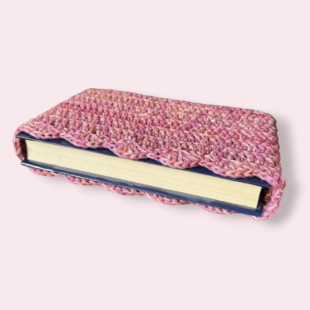 Pink crochet book sleeve with book inside on plain background