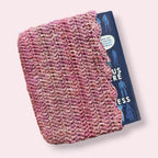 Pink crochet book sleeve with book peeking out on plain background