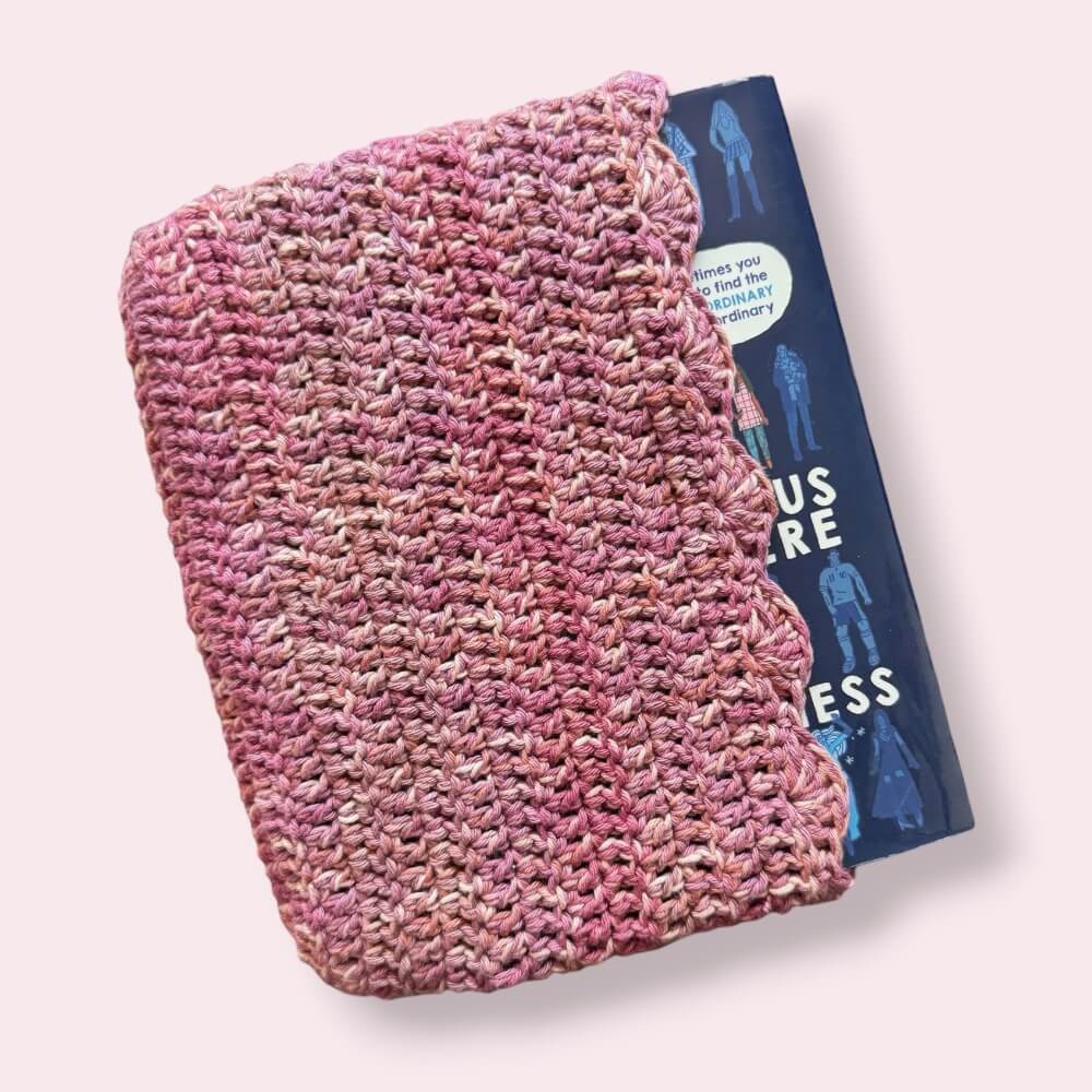 Pink crochet book sleeve with book peeking out on plain background
