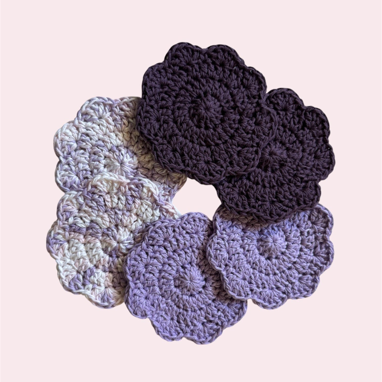 Set of crocheted coasters in various purple colors on a pink background
